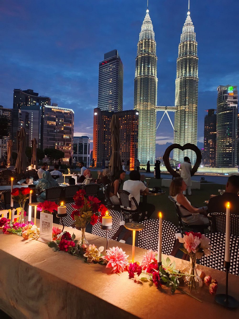 Candlelit dusk table with flowers and guests dining beside the lit Petronas Towers